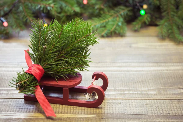 Saco rojo navideño con regalos en trineo sobre fondo de madera con ramas de abeto y guirnaldas . — Foto de Stock