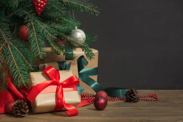 Noel tatil arka plan. Hediyeler bir kırmızı kurdele, Noel Baba'nın şapka ve dekor ahşap bir gemide bir Noel ağacı altında. — Stok fotoğraf