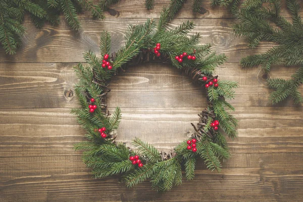 Christmas wreath of spruce branches with holly berries on wooden board. Flat lay. Top view.
