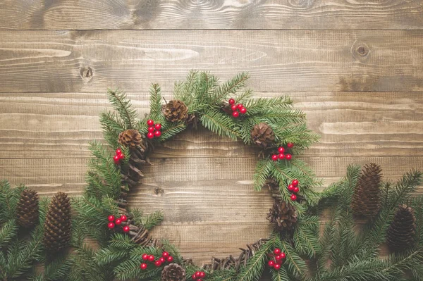 Karácsonyi koszorú a fenyő ágak holly bogyók fából készült táblán. Lapos feküdt. Felülnézet. Tónusú kép. — Stock Fotó