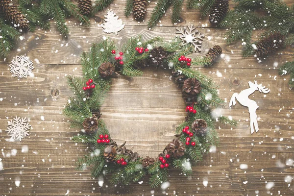 Christmas wreath of spruce branches with holly berries on wooden board. Flat lay. Top view.