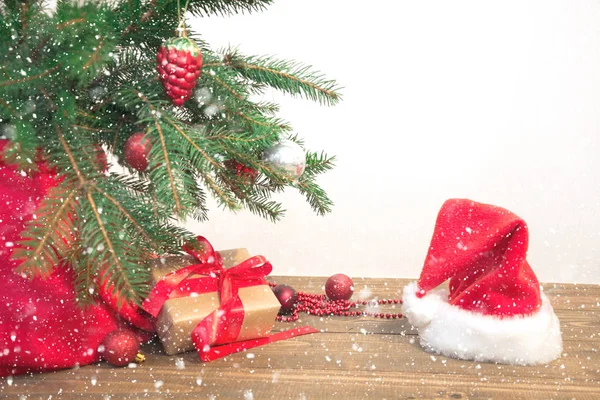 Fondo de vacaciones de Navidad. Regalos con una cinta roja, sombrero de Santa Claus y decoración bajo un árbol de Navidad en una tabla de madera. Copiar espacio en blanco . — Foto de Stock