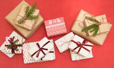 Christmas gifts wrapped in ornament paper and decorative red rope ribbon on red surface. Creative hobby, top view. Prepare to Xmas. clipart