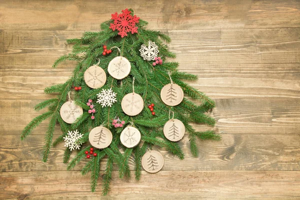 Árbol de Navidad hecho de rama de abeto rebanada de madera decorada, copos de nieve, bayas de acebo en tablero de madera. Vista superior y espacio para texto . — Foto de Stock