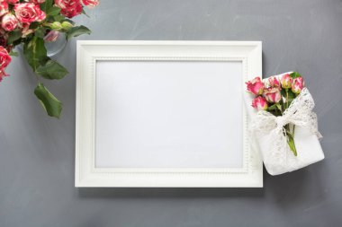 Kadın hediye ve gri arka plan üzerinde küçük gül beyaz fotoğraf çerçevelemek. Üstten Görünüm. Kopya alanı.