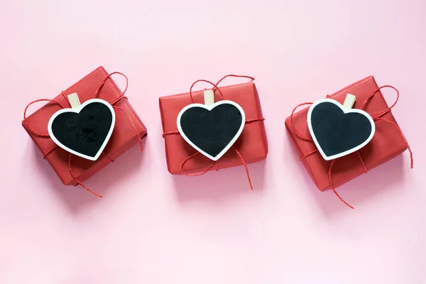 Composición San Valentín: tres cajas de regalo rojas con pinza como corazón con espacio para texto sobre pizarra sobre fondo rosa pastel. Vista desde arriba . —  Fotos de Stock