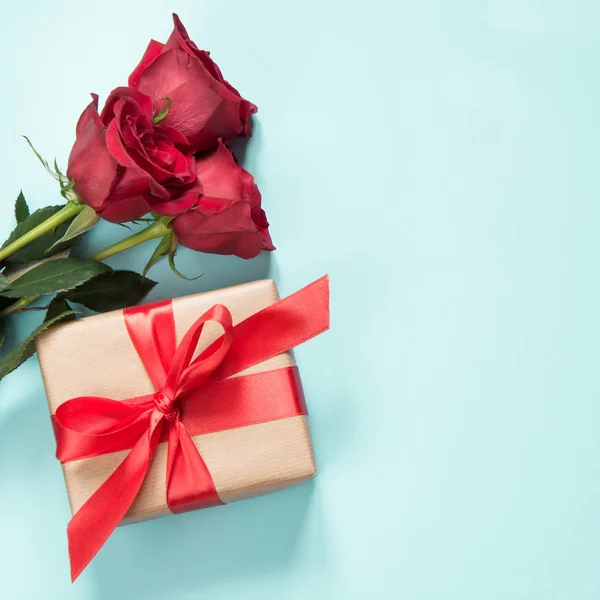 Boeket van rode rozen en gift met rood lint op pastel blauwe achtergrond. Valentijnsdag kaart. Close-up. Kopiëren van ruimte. — Stockfoto