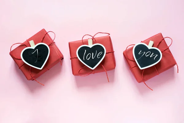 Composición San Valentín: tres cajas de regalo rojas con pinza como corazón con texto sobre pizarra sobre fondo rosa pastel. Vista desde arriba . —  Fotos de Stock