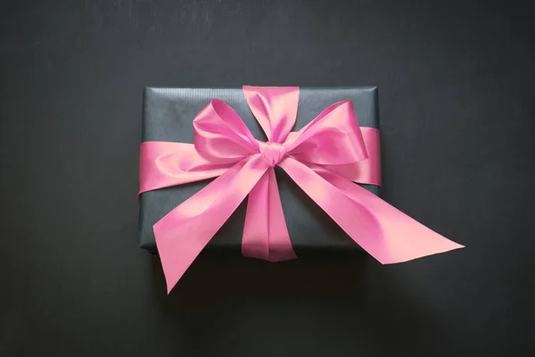 핑크 리본 블랙 표면에 검은 종이에 싸서는 선물 상자. 위에서 볼 수 있습니다. 공간 복사. — 스톡 사진
