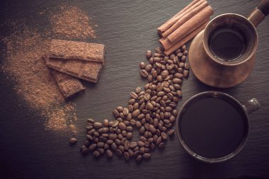 Bir fincan sade kahve, kahve çekirdekleri, çikolata, tarçın ve eski cezve üzerinde kopya alanı ile arka plan olarak siyah arduvaz kaplamak. Tonlu görüntü.