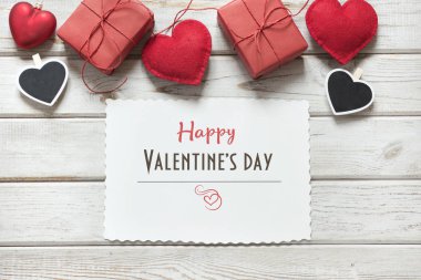 Sevgililer günü kartı. Kırmızı dekor, kupa, hediyeler, beyaz levha ile clothespin ve metin üzerinde beyaz ahşap tahta istiyor. Yukarıdan görüntülemek.