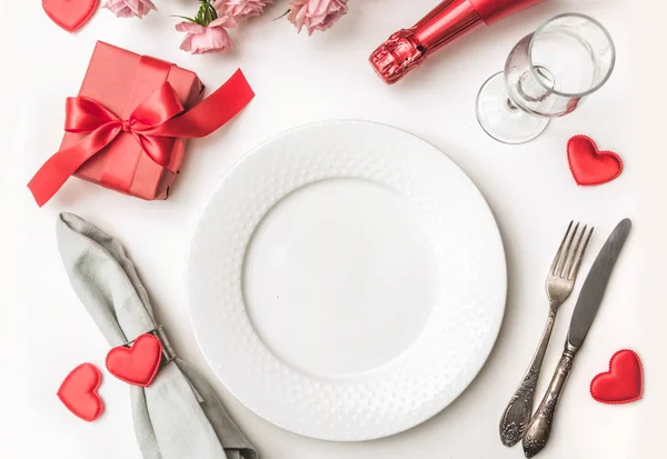 День святого Валентина ужин с сервировкой стола с красным подарком, бутылка шампанского, сердца с серебром на белом фоне. Вид сверху. Открытка Валентина . — стоковое фото