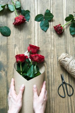 Çiçekçi bir kırmızı gül buketi, kraft Kağıt ahşap bir masa üzerinde kaydırma yapma. Yukarıdan görüntülemek.