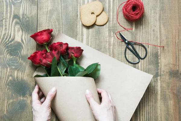 Floristería haciendo un ramo de rosas rojas, envolviendo en papel kraft sobre una mesa de madera. Vista desde arriba . — Foto de Stock