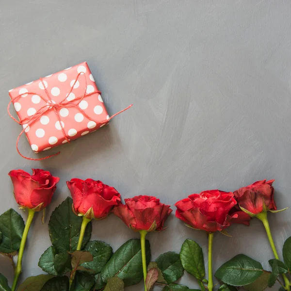 Rode rozen en huidige gift op grijze achtergrond. Valentijnsdag kaart. Close-up. Kopiëren van ruimte. — Stockfoto