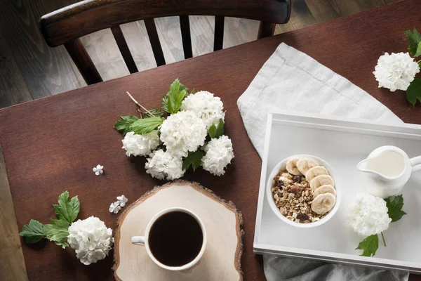 Ein gesundes Frühstück mit einer Tasse Kaffee, Müsli, Bananen und Dekor mit Viburnumblumen in einem Landhaus. — Stockfoto