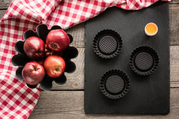 Manzanas rojas maduras en tablero de madera con toalla a cuadros roja alrededor y accesorios para hornear . —  Fotos de Stock