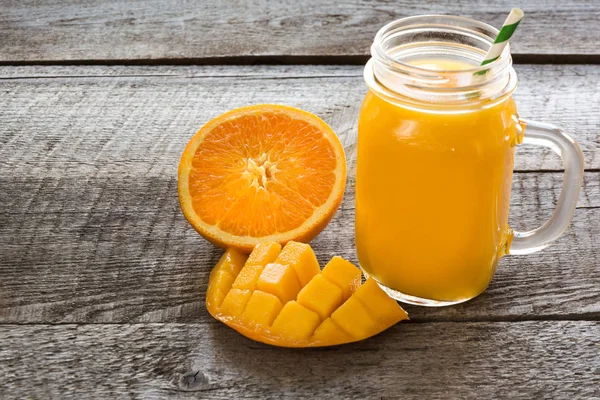 Zumo tropical con frutas: mango, naranja en un frasco de albañil de vidrio en el tablero de madera viejo . — Foto de Stock