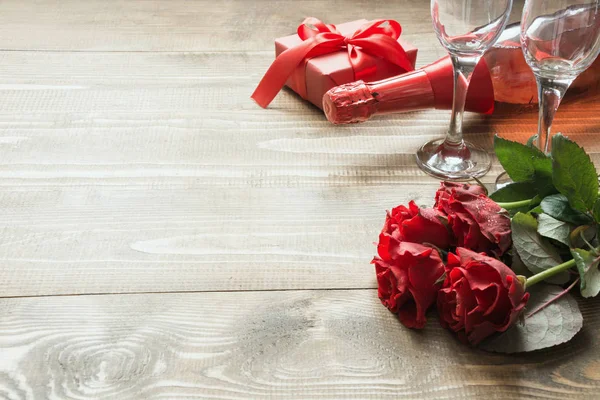 Tarjeta de felicitación de San Valentín con flores de ramo de rosas rojas, una botella de champán y caja de regalo en la mesa de madera. Copiar espacio . — Foto de Stock