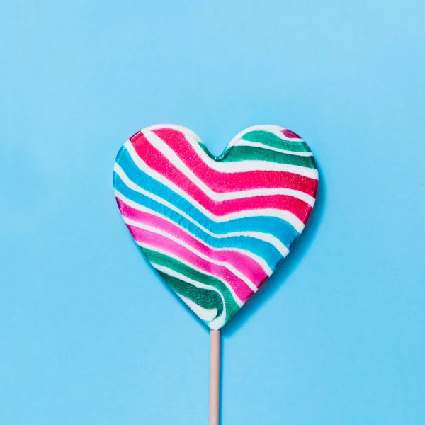 Lollipops arcobaleno colorato caramelle a strisce come il cuore sul blu. Concetto divertente. Vista dall'alto. Immagine quadrata . — Foto Stock