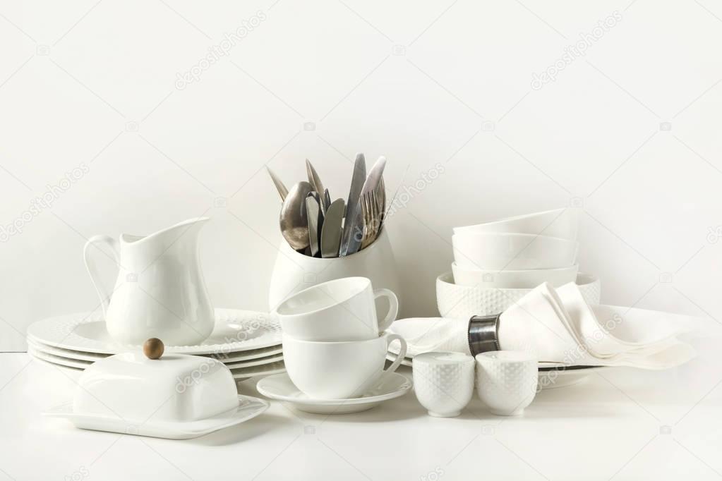 White tableware for serving. Crockery,dish, utensils and other different white stuff on white table-top. Kitchen still life. Copy space.