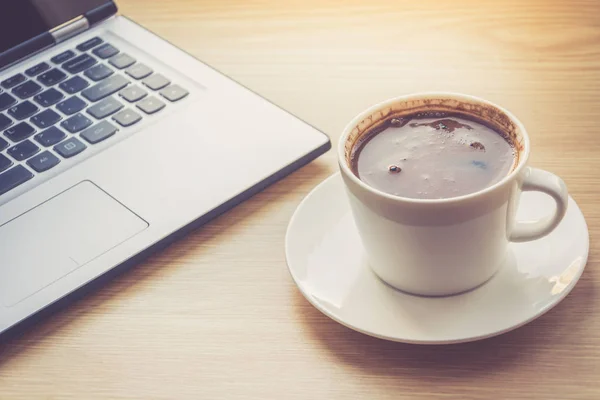 Stäng upp syn på arbete skrivbord interiör med bärbar dator och morgon kaffe kopp. Tonad foto av skrivbord med dator och kaffekopp. — Stockfoto