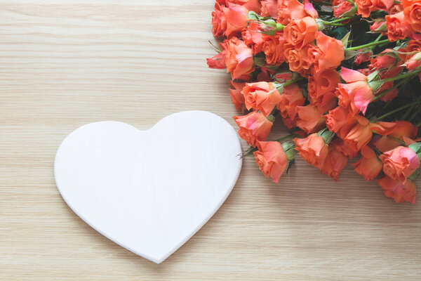 Spring concept. Bouquet of orange roses with white heart as blank on wooden board. Top view. Romantic or Valentine's card. Copy space.