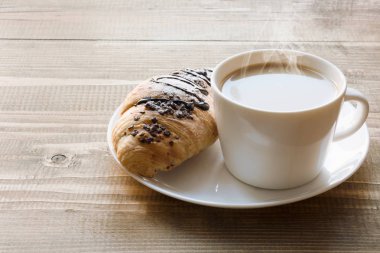 Fırından yeni çıkmış çikolatalı kruvasan ve kahve ahşap tahta üzerinde. Kahvaltı konsepti.