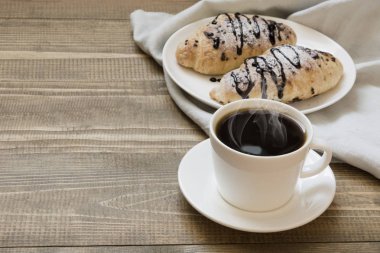 İki çikolatalı kruvasan ve kahve ahşap tahta üzerinde fırından yeni çıkmış. Kahvaltı konsepti.