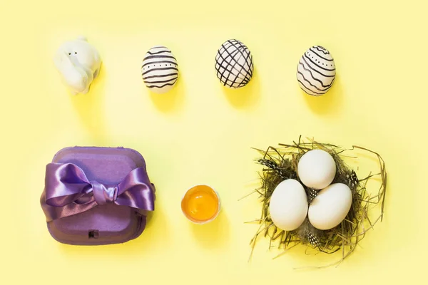 Creatief Pasen samenstelling met beschilderde eieren, violet doos en nest, op gele achtergrond. Plat leggen. — Stockfoto