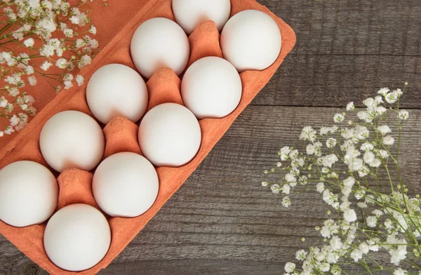 Colorful carton of organic white eggs with flower on wooden board. Top view.