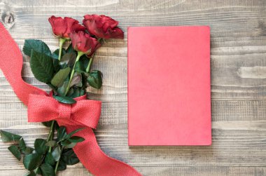 Buket kırmızı gül ve kırmızı defter ahşap tahta üzerinde. Kopya alanı.