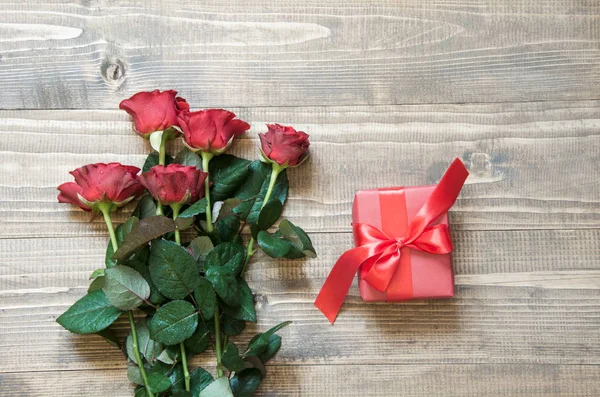 Ramo de rosas rojas con regalo en tabla de madera. Vista superior . — Foto de Stock