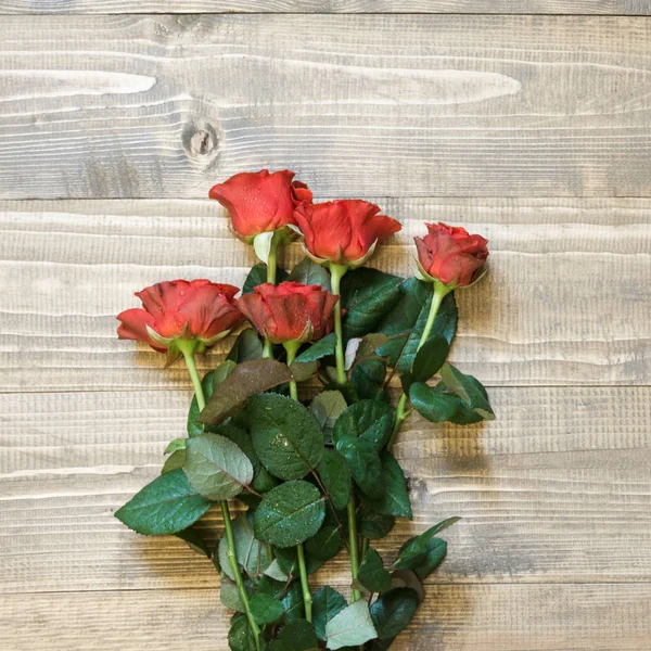 Tarjeta de San Valentín. Rosas rojas envueltas en papel sobre fondo de mesa de madera. Vista superior . — Foto de Stock