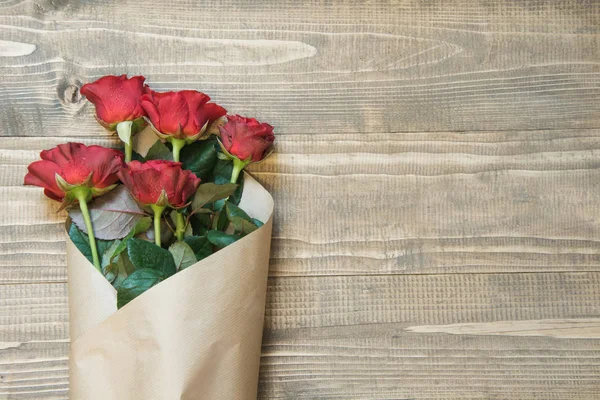 Ramo de rosas rojas envueltas en papel sobre tabla de madera. Vista superior . — Foto de Stock