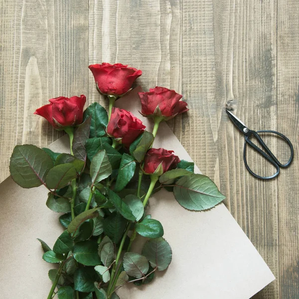 Флорист делает букет из красных роз, завернутый в крафтовую бумагу на деревянном столе. Вид сверху. Сельский стиль . — стоковое фото