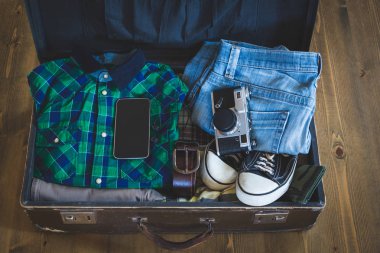 Vintage hipster seyahat ambalaj açık bavul giyim, film-kamera ve cep ile ahşap bir gemide