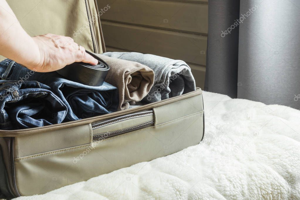 A man handles things. View to the bedroom. Open suitcase with clothes on bed.