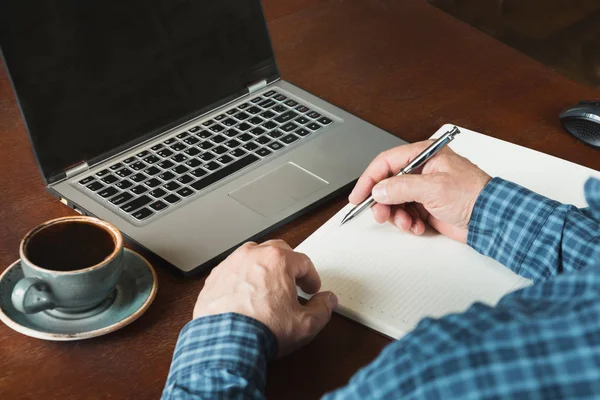 Задний вид, снятый руками занятого бизнесмена, пишущего ручкой и использующего ноутбук на рабочем столе . — стоковое фото