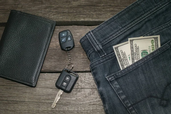 Carteira preta, chave de carro e dólar americano em jeans na placa de madeira . — Fotografia de Stock