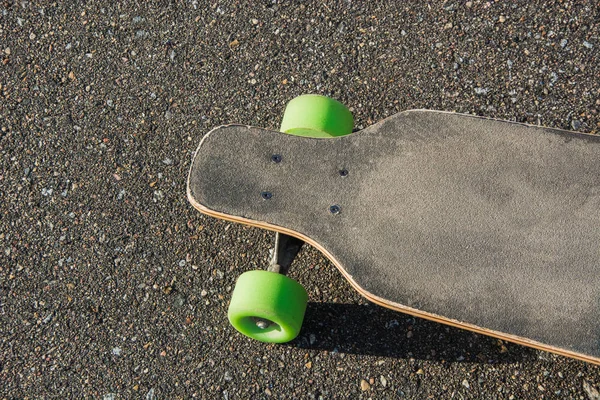 Old used longboard isolated on the ground. Black skateboard on an empty asphalt road. — Stock Photo, Image