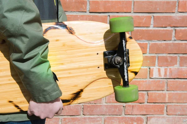 Teen drží longboard cihlové zdi. Detailní záběr. — Stock fotografie
