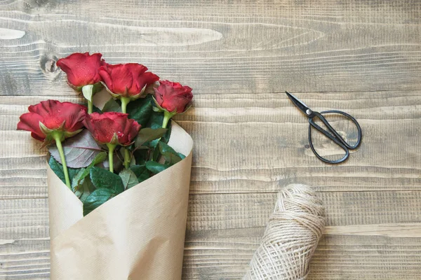 Envolvendo um buquê de rosas vermelhas na mesa de madeira. Vista de cima. Estilo rústico. Vista superior . — Fotografia de Stock
