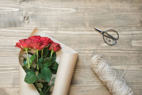 Een rode rozen boeket te verpakken op houten tafel. Bekijk van bovenaf. Rustieke stijl. Bovenaanzicht. — Stockfoto