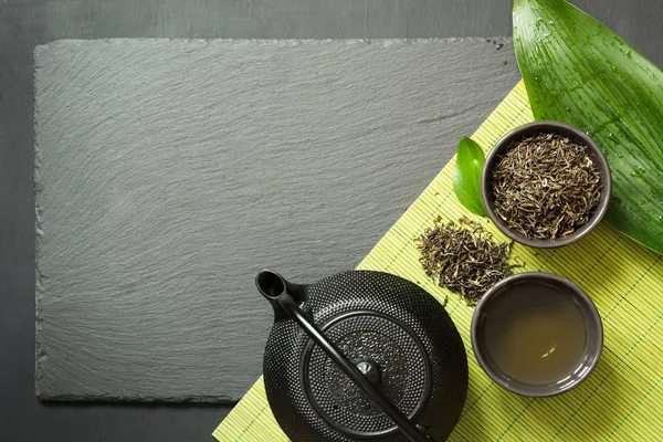 Té verde japonés sobre fondo de pizarra negra. Tetera negra y tazón con té verde. Vista superior con espacio de copia . —  Fotos de Stock