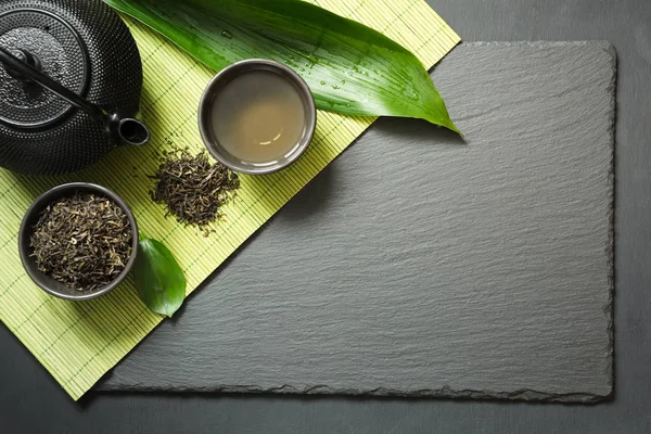 Té verde japonés sobre fondo de pizarra negra. Tetera negra y tazón con té verde. Vista superior con espacio de copia . —  Fotos de Stock