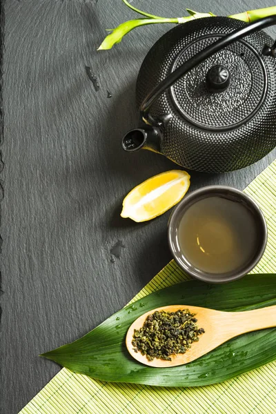 Té verde japonés sobre fondo de pizarra negra. Tetera negra y tazón con té verde. Vista superior con espacio de copia . —  Fotos de Stock