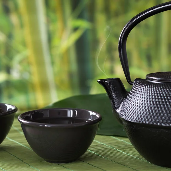 Taza con té verde con hervidor de agua de porcelana negra sobre fondo borroso naturaleza. De cerca. . —  Fotos de Stock