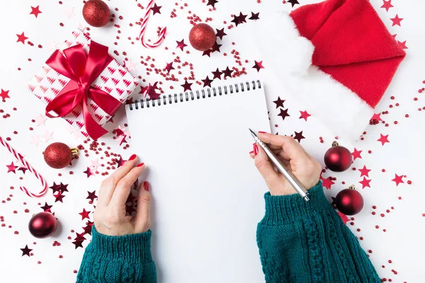 Mujer en jersey verde escribiendo una lista de planes y sueños para el próximo año. Lista de deseos para Navidad. Lista de tareas para Nuevo 2020 año con la decoración roja de vacaciones . —  Fotos de Stock