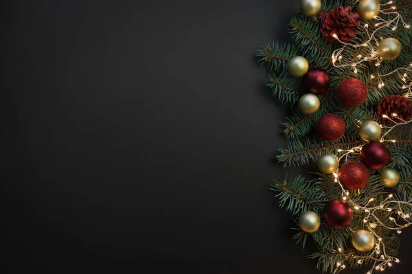 Marco de Navidad con ramas de abeto, bolas rojas y doradas, guirnalda de Navidad sobre fondo negro. Espacio para texto, vista desde arriba, plano. Banner . —  Fotos de Stock